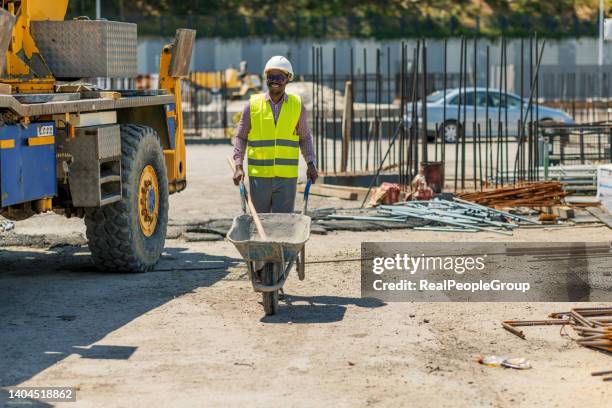 operaio edile che spinge il tumulo in cantiere - carriola foto e immagini stock