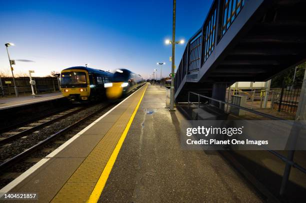 Old and new - streamlined passenger train passes older model in Radley Station during dusk.