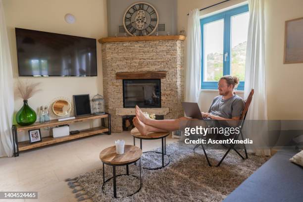 young man works on laptop, in living room - early access stock pictures, royalty-free photos & images