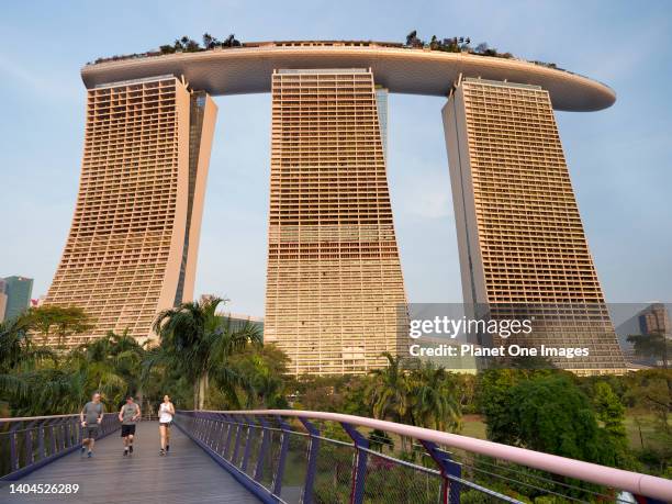 Gardens by the Bay, Singapore - 3 - 5 March 2019; three joggers in shot. The iconic three-towered Marina Bay Sands Hotel, opened in 2010, is a luxury...