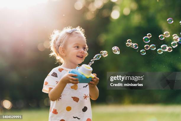 cheerful young girl having fun in the park making and bursting bubbles - bellenblaas stockfoto's en -beelden