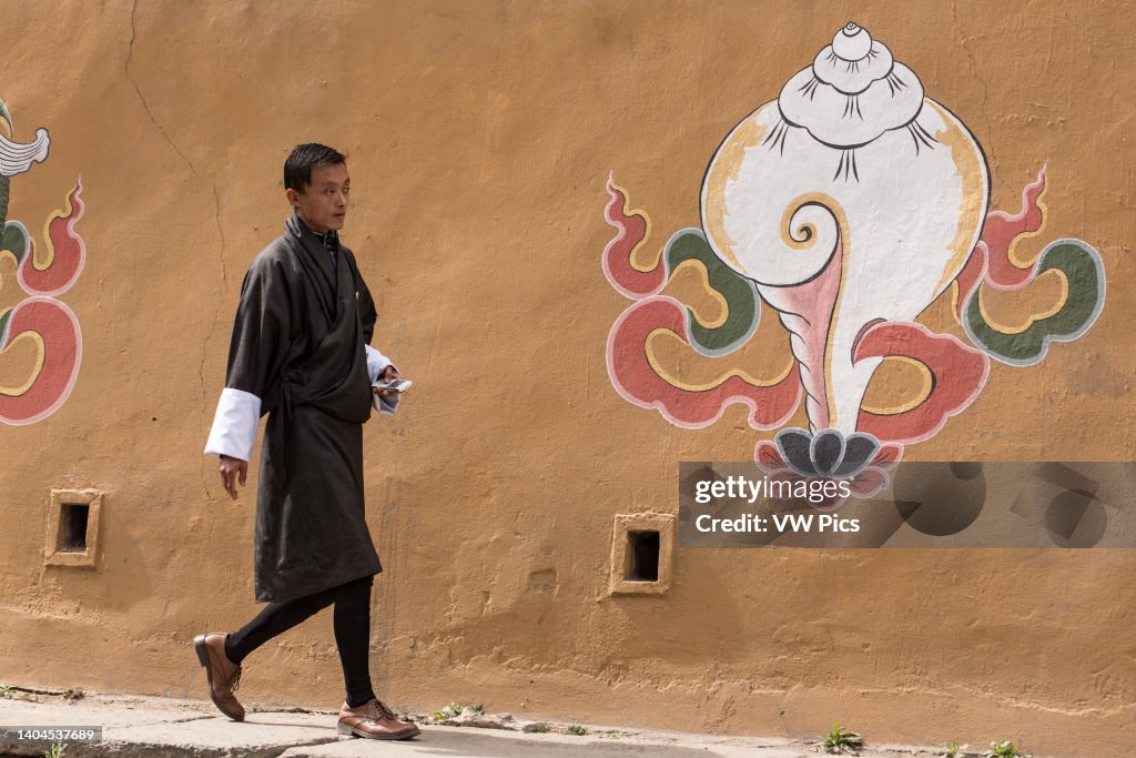 A young Bhutanese man walks past Buddhist religious art painted on a wall in Thimphu
