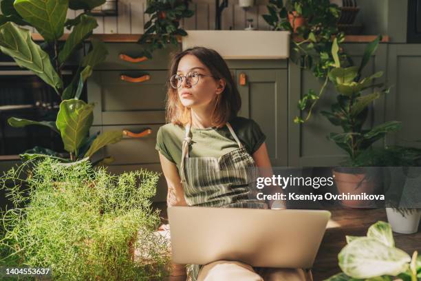 freelance woman in glasses with mobile phone typing at laptop and working from home office. happy girl sitting on couch in living room with plants. distance learning online education and work. - teen entrepreneur stock pictures, royalty-free photos & images