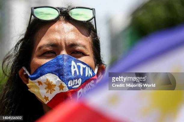 Metro Manila, Philippines. 12th June 2021. A woman wears a mask bearing the Philippine flag with a sign 'Atin Ang Pinas' during a protest marking...