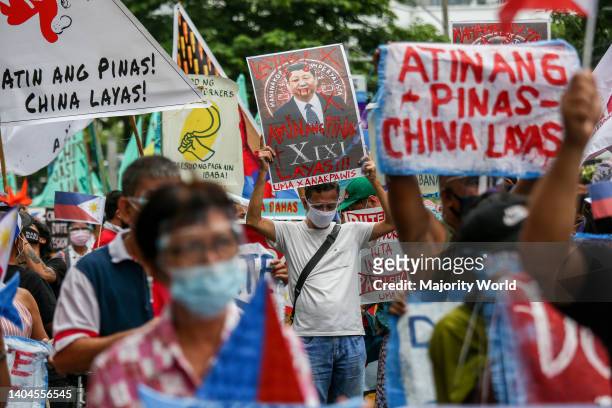 Metro Manila, Philippines. 12th June 2021. Activists carry signs and Philippine flags as they gather to protest in front of the Chinese consulate...