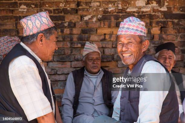 Group of Nepali men in traditonal Dhaka topi caps rest in the shade and visit in the medieval city of Bhaktapur, Nepal.