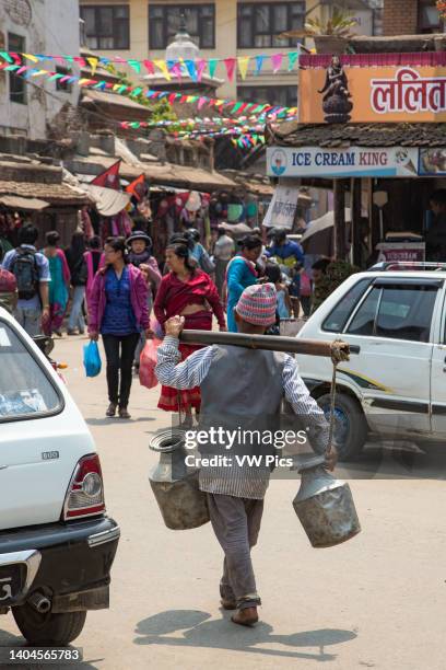 Nepali man carrying metal milk cans on a shoulder yoke on the street in Patan, Nepal.