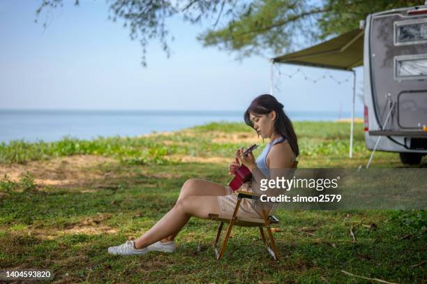 junge asiatische frau spielt gitarre neben ihrem wohnmobil am strand - liedermacher stock-fotos und bilder