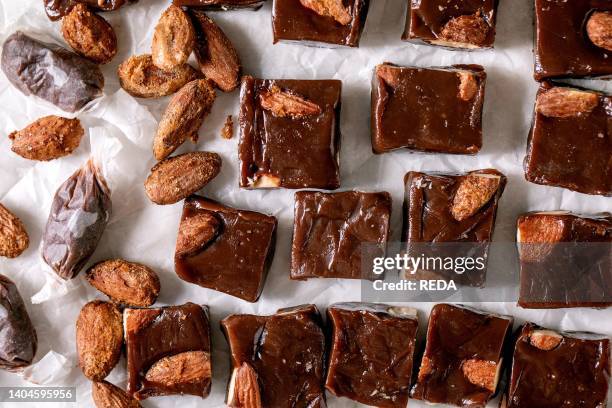 Homemade toffee salted caramel chocolate almond nuts candy on crumpled paper in row over white linen tablecloth. Handmade food sweet gifts for any...