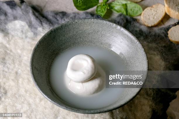 Traditional italian burrata knotted cheese in grey ceramic bowl on table. Bread, olives, greens around. Ingredients for healthy mediterranean dinner..
