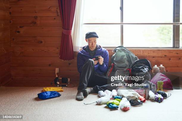 asiatischer mann mit smartphone in einer berghütte, um sich auf den morgigen kletterplan vorzubereiten. - berghütte stock-fotos und bilder