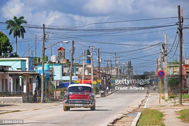 Red American classic car driving through the town Jatibonico, Sancti Spíritus Province on the island Cuba, Caribbean.