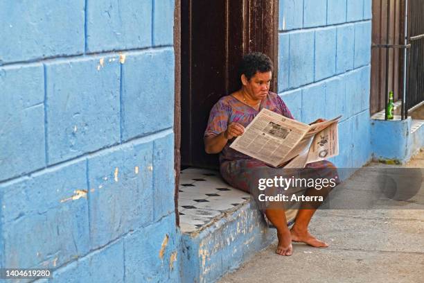 Cuban woman reading the Trabajadores, weekly Cuban trade union newspaper on the doorstep of her house in the city Sancti Spíritus on the island Cuba.