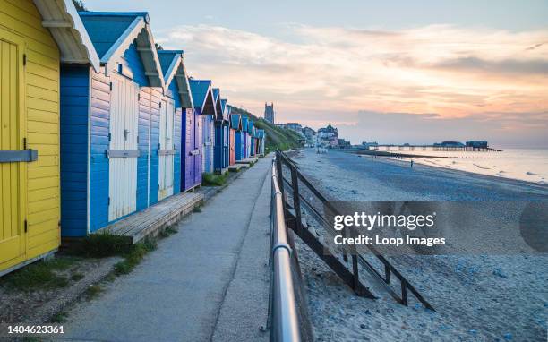 Pretty beach huts lined up on the East beach of Cromer seafront leading to the pier.