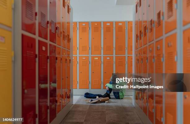 sad boy sitting in the floor in locker room. - bully school stock-fotos und bilder