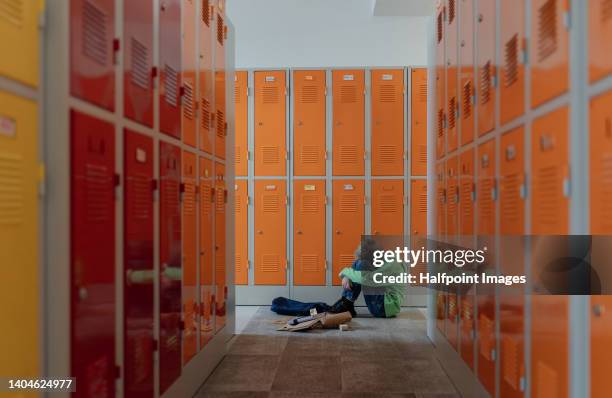 sad boy sitting in the floor in locker room. - violencia escolar fotografías e imágenes de stock