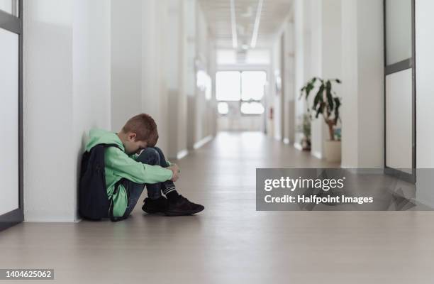 sad little boy sitting in school corridor. - cyberbullying stock pictures, royalty-free photos & images