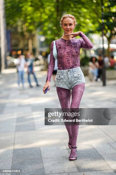 Olga Karput wears gold earrings, a pink and purple denim print pattern long sleeves jumpsuit, blue faded denim quilted shorts, a pale blue matte...