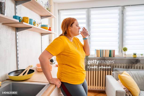 young overweight woman drinking water after exercising at home - plus size stock pictures, royalty-free photos & images