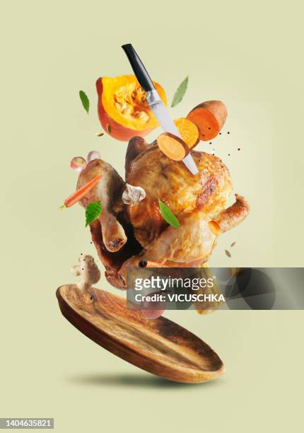 creative thanksgiving food with whole roasted turkey, sweet potato, knife, carrot, pumpkin, onion, garlic and herbs flying in the air over wooden plate at pale beige background. - thanksgiving plate of food fotografías e imágenes de stock