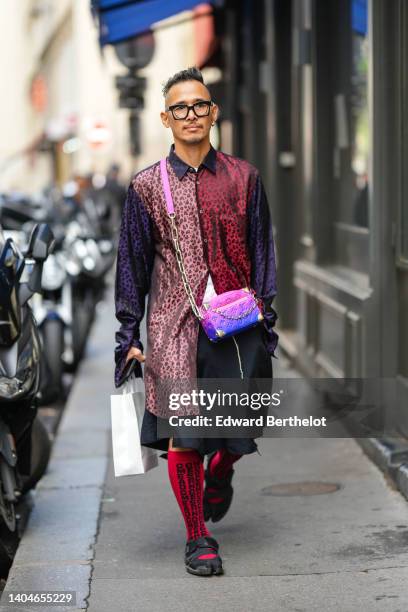 Guest wears black sunglasses, silver earrings, a burgundy / pale pink / purple and black leopard print pattern oversized silk shirt, a white shirt,...