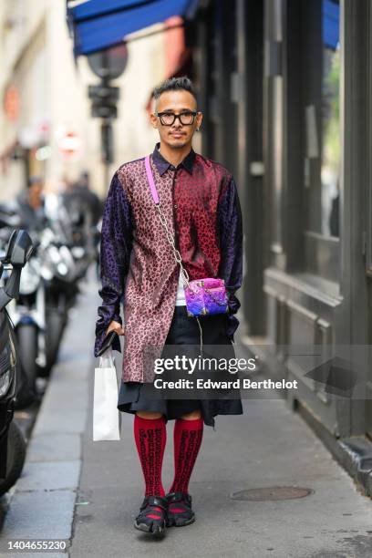 Guest wears black sunglasses, silver earrings, a burgundy / pale pink / purple and black leopard print pattern oversized silk shirt, a white shirt,...