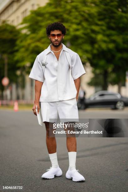Guest wears orange sunglasses from Givenchy, a white pearls necklace, a white oversized short sleeves / oversized shirt, matching white suit shorts,...