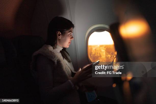 mujer que viaja en avión y mira a través de la ventana y usa el teléfono móvil - aircraft wifi fotografías e imágenes de stock