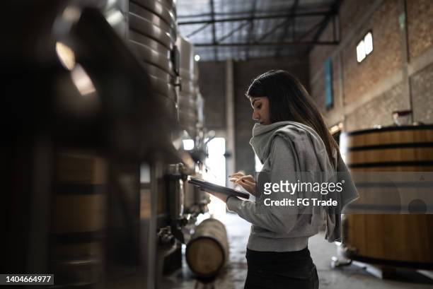mujer medianamente adulta trabajando en una tableta digital en una bodega - wine maker fotografías e imágenes de stock
