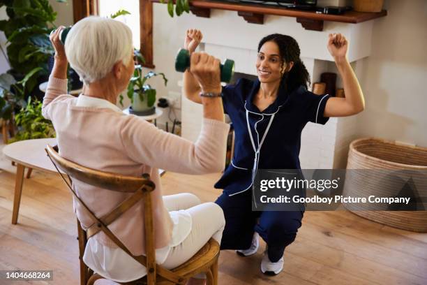 smiling physical therapist teaching a senior woman exercises with weights at home - injury prevention stock pictures, royalty-free photos & images