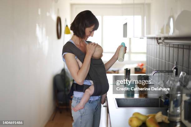 a 6 month old baby boy and his mum at home, she's preparing his baby bottle in the kitchen - 6 11 monate stock-fotos und bilder