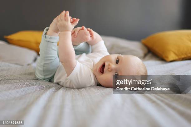 a 6 month old baby boy smiling, laying on a bed - white bed cushion stock-fotos und bilder