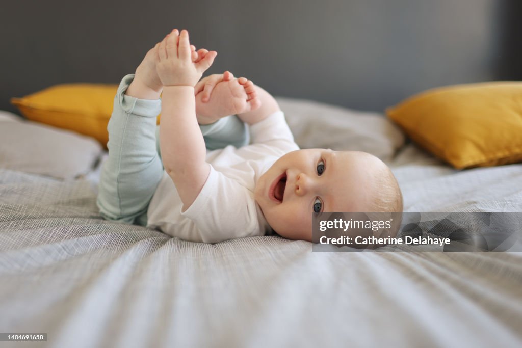 A 6 month old baby boy smiling, laying on a bed