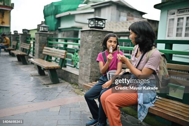 mother and daughter sitting on a bench and enjoying ice cream candy - indian mother and child stock pictures, royalty-free photos & images