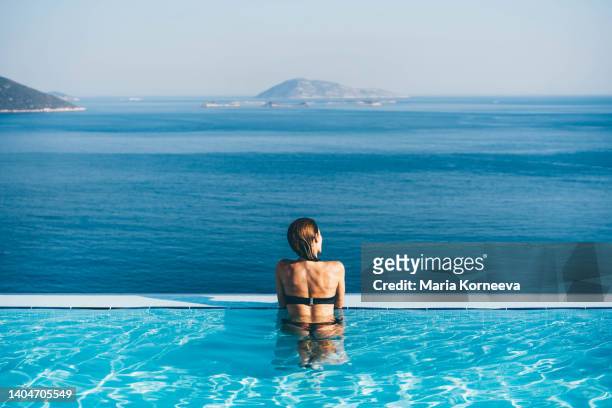 woman in infinity pool admiring scenic view. - woman pool relax stockfoto's en -beelden