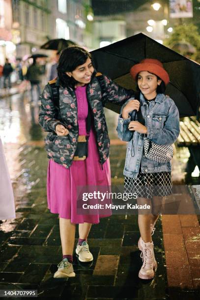 mother and daughter walking on a street in rains holding umbrella - enjoy monsoon stock-fotos und bilder