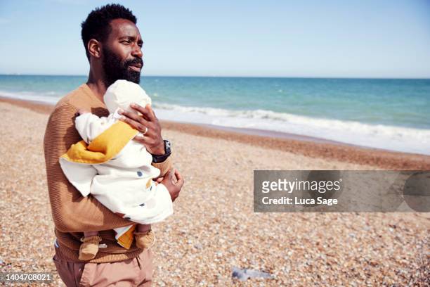 Father lovingly holding his newborn baby daughter on the beach, a road trip in the off season.