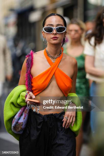 Guest wears silver earrings, silver sunglasses, a silver large necklace, a gold chain pendant necklace, a neon orange ribbed halter neck / cropped...