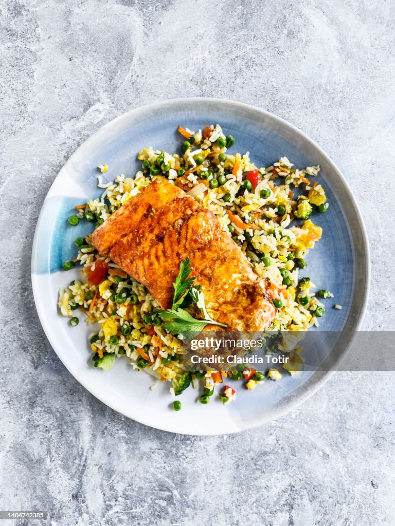 Plate of fried rice with roasted salmon on gray background