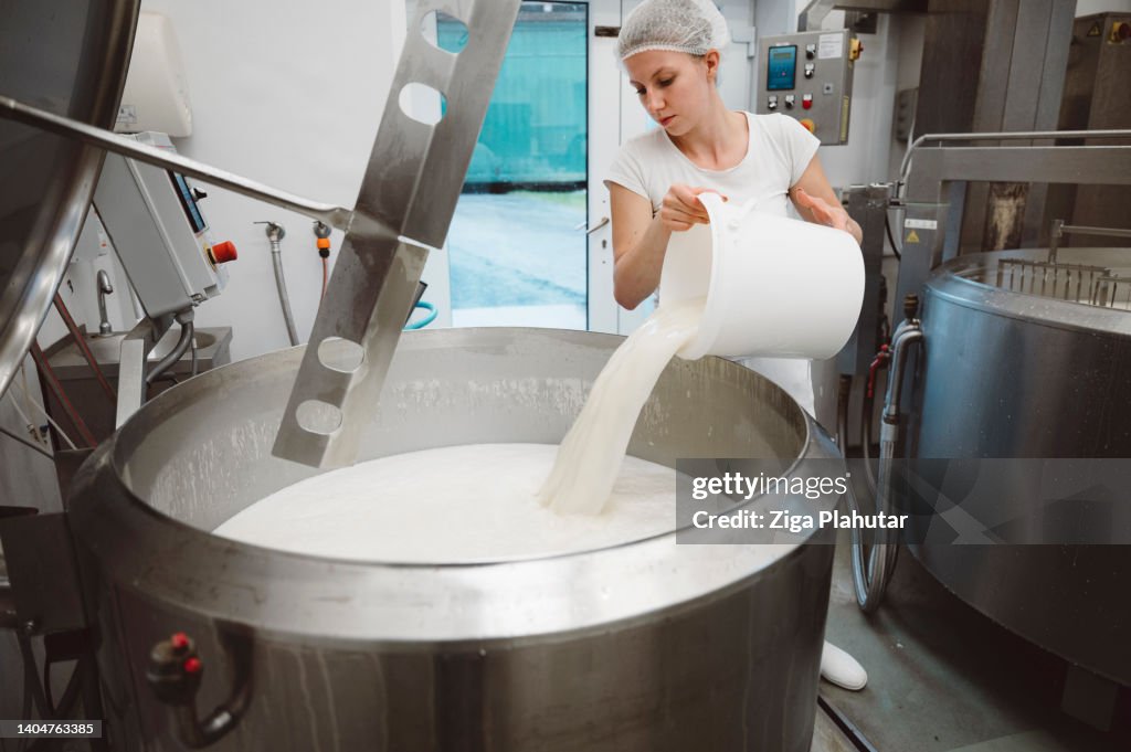 Woman pouring a bucket of milk in a large industrial pot