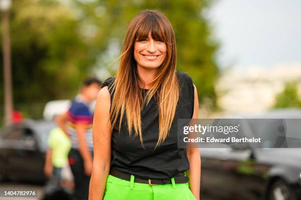 Caroline de Maigret wears a black sleeveless t-shirt, a black shiny leather belt, neon green large pants, outside the AMI show, during Paris Fashion...