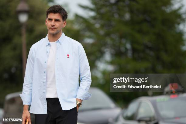 Johannes Huebl wears a white t-shirt, a pale blue open shirt with embroidered red logo shirt from Ami, black sunglasses, a gold watch, outside the...