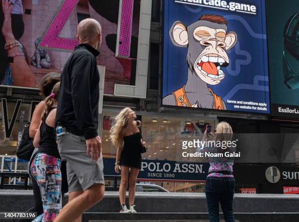 People take photos by a Bored Ape Yacht Club NFT billboard in Times Square during the 4th annual NFT.NYC conference on June 23, 2022 in New York...