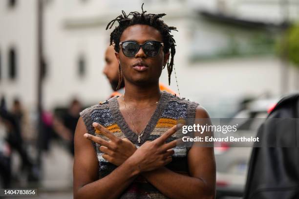 Kailand Morris wears black sunglasses, a brown / gray / orange striped print pattern sleeveless pullover, gold long pendant necklace, outside the...