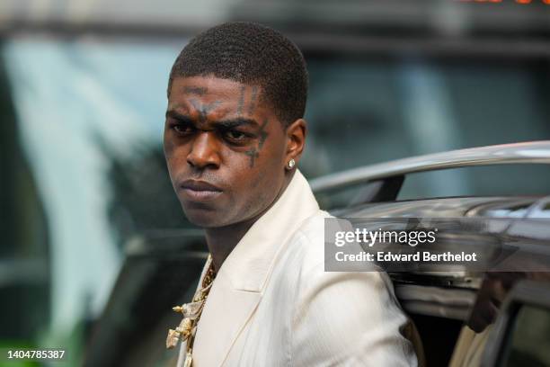 Kodak Black wears diamond earrings, oversized large pendant chain necklaces, a white latte blazer jacket, outside the Amiri show, during Paris...