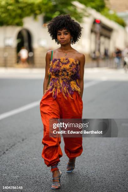 Sarah Monteil wears multicolored pearls earrings, a gold chain necklace, a purple and orange print pattern / shoulder-off fluffy top, a green shiny...