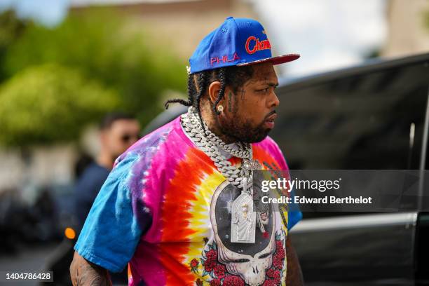Westside Gunn wears a royal blue with embroidered orange pattern cap, gold and diamond earrings, a silver and diamond large chain necklace and large...
