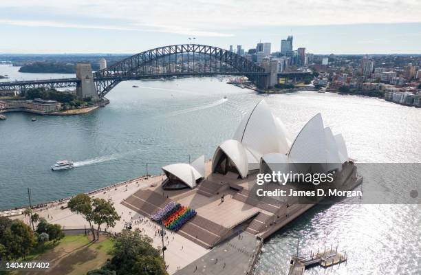 In this aerial view, a group of people form a progress flag at the Sydney Opera House on June 24, 2022 in Sydney, Australia. 1,000 Sydneysiders...