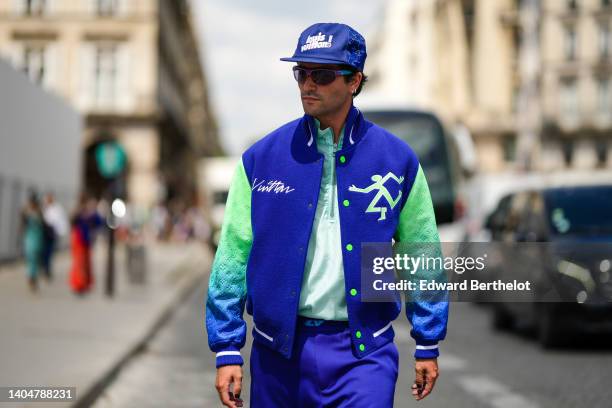 Marc Forne wears royal blue with embroidered white pattern cap from Louis Vuitton, purple sunglasses, silver earrings, a pale green t-shirt, a royal...