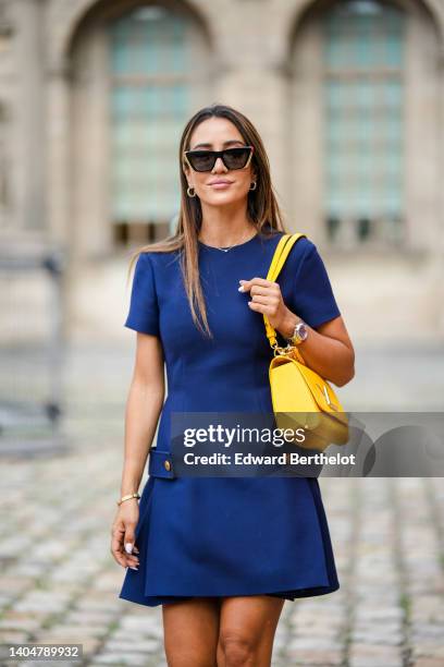 Tamara Kalinic wears sunglasses from Louis Vuitton, gold earrings, a silver with diamond pendant necklace, a navy blue short sleeves / buttoned short...